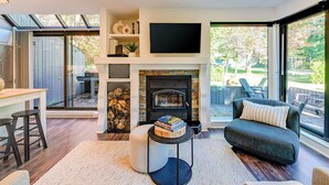 Ein modernes Wohnzimmer mit Kamin, einem flachbildfernseher darüber und einer gemütlichen Sitzecke mit Sofa und Hocker.