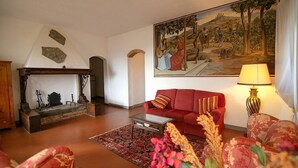 Un soggiorno con camino, un divano rosso, un quadro e una lampada.