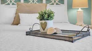 A bed with a decorative tray, a heart-shaped mug with a plant, and seashells. - 2 min walk to the beach from our Ocean Escape Jax Beach 3BR home! (Jacksonville Beach)
