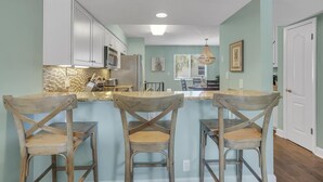 A kitchen with white cabinets, a granite countertop, and a central island with bar stools. - 2 min walk to the beach from our Ocean Escape Jax Beach 3BR home! (Jacksonville Beach)