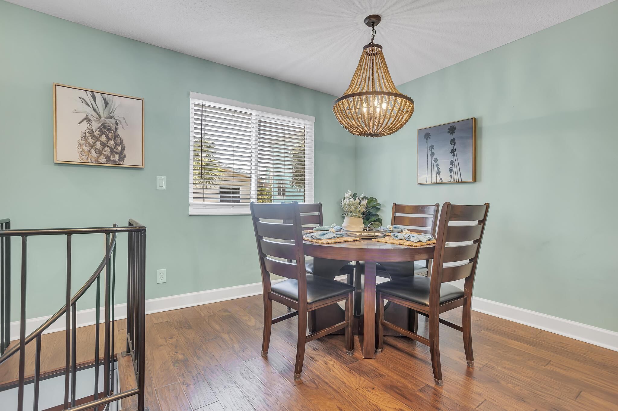 A dining area with a round table, four chairs, a chandelier, and artwork on the walls.