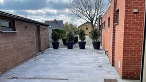 A paved courtyard with potted plants, brick buildings, and a clear sky. - Cozy holiday home 't Sevencoote - terrace - private parking (Gistel)