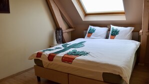 A bed with a white bedspread and two pillows, one with a cactus design, in a room with a sloped ceiling and a skylight. - Cozy holiday home 't Sevencoote - terrace - private parking (Gistel)
