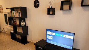 Un salon comprenant un téléviseur, une bibliothèque, une horloge et une petite table ornée d’un objet décoratif.