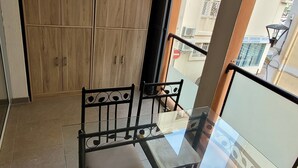 Un balcon avec une table et des chaises en verre, une armoire en bois et une vue sur le paysage urbain.
