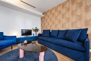 Un salon moderne avec un canapé bleu, une table basse noire et un téléviseur posé sur un meuble blanc.