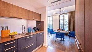 Una cocina moderna con un lavamanos, una cafetera y un cuenco de fruta. Hay una zona de comedor con sillas azules y una mesa.