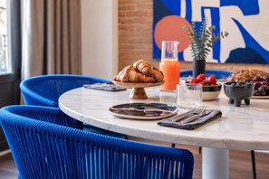 Een ontbijt met croissants, een glas sinaasappelsap, aardbeien en een schaaltje bosbessen op een marmeren tafel.