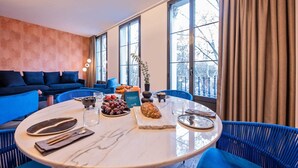 Un comedor moderno con una mesa redonda de mármol, sillas tapizadas en azul y vistas a árboles a través de amplios ventanales.