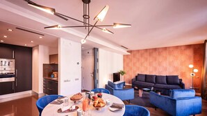 Ein modernes Wohnzimmer mit einem blauen Sofa, einer Essecke mit rundem Tisch und einer Küche mit Einbauofen.