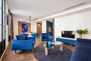 Een moderne woonkamer met blauw meubilair, een flatscreen televisie en een eethoek met een accentmuur van baksteen.