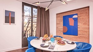 Ein Essbereich mit einem runden Tisch, blauen Stühlen und einer Ziegelwand mit abstrakter Kunst.