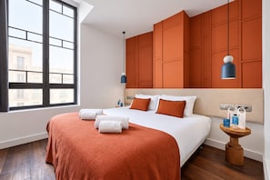 Een hotelkamer met een groot bed, een houten vloer, een raam met uitzicht op gebouwen en een wand met een gepaneeld ontwerp.