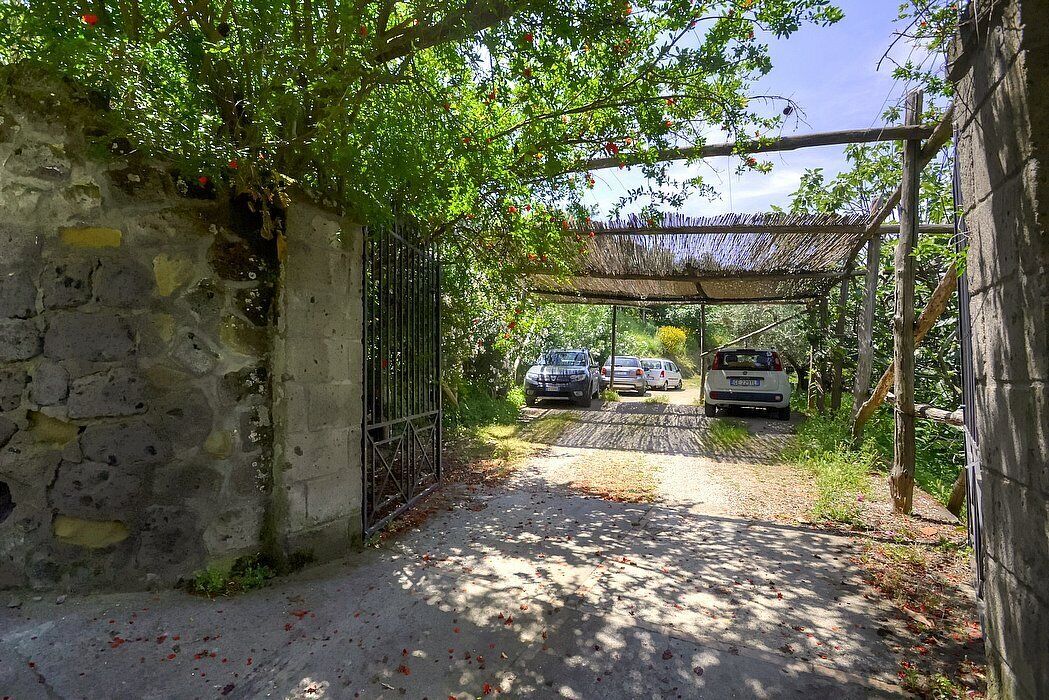 A stone wall with a metal gate, a covered pathway, and parked cars.