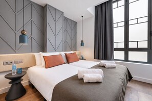 Een hotelkamer met een bed, nachtkastjes, een raam met gordijnen en een geometrisch wandontwerp.