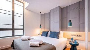 Une chambre d’hôtel moderne avec un grand lit, deux tables de chevet, une fenêtre et un luminaire fixé au mur.