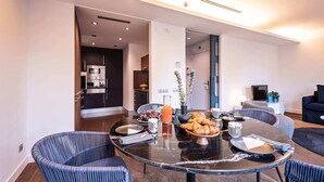 Un espace repas moderne avec une table ronde en verre, deux chaises bleues à revêtement rembourré et une cuisine en arrière-plan.