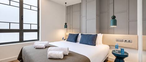 Una habitación de hotel moderna con una cama grande, dos mesitas de noche, un ventanal y un aplique de pared.