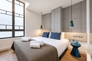Een moderne hotelkamer met een groot bed, twee nachtkastjes, een raam en een wandlamp.
