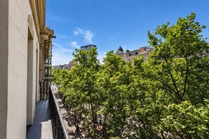 Un balcon donnant sur une rue bordée d’arbres, avec des immeubles en arrière-plan.