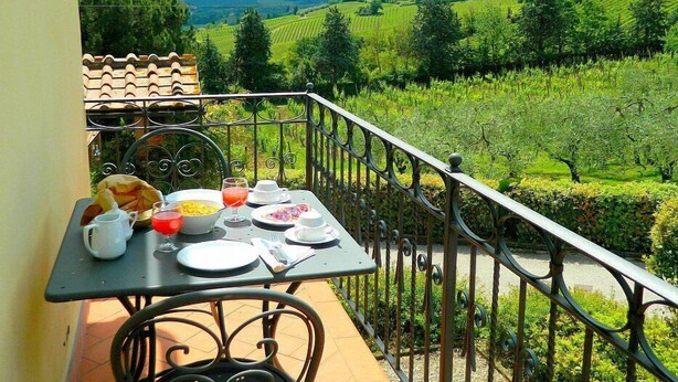 A balcony with a table set for breakfast, overlooking a vineyard.