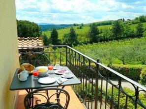 A balcony with a table set for breakfast, overlooking a vineyard. - Appartamento Reginaldo D: A cozy apartment that is part of a villa in the characteristic style of the Tuscan countryside, with Free WI-FI. (San Gimignano)