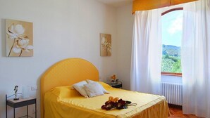 A bedroom with a bed, a nightstand, a window with curtains, and two wall-mounted flower paintings.