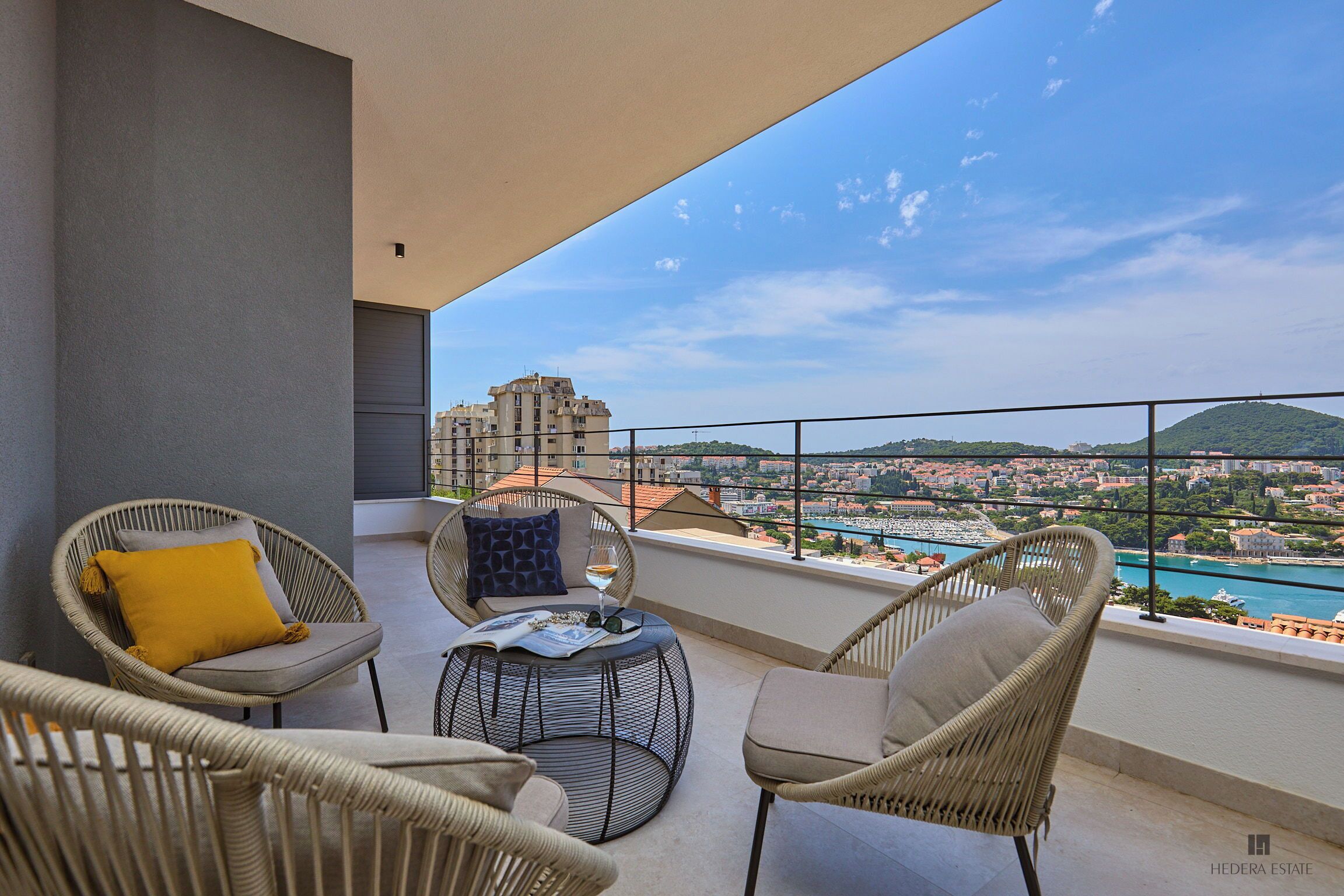 Un balcon avec des fauteuils en osier, une table ronde et une vue sur le paysage urbain et la rivière.