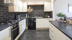 A modern kitchen with black and white tiles, stainless steel appliances, and wooden cabinets. - 4 Pen Llanw Tides Reach (Rhosneigr)