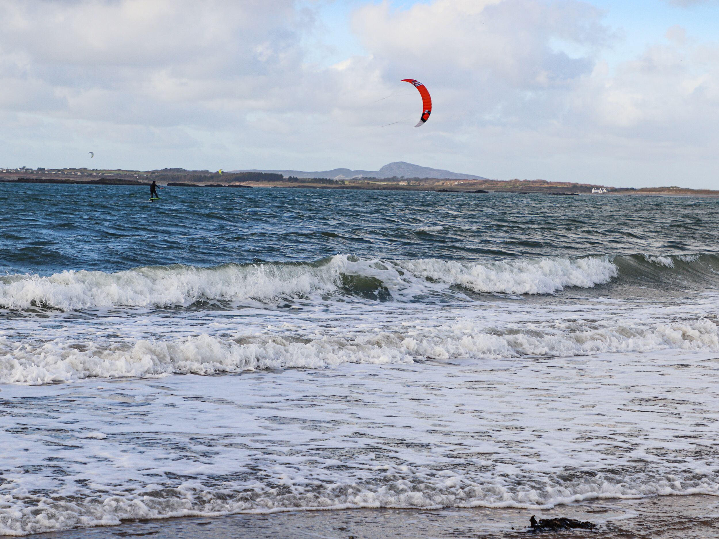 Platja amb ones i una persona fent kitesurf.