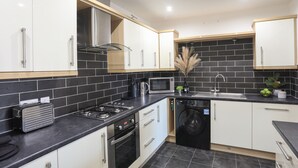 A modern kitchen with white cabinets, a black tiled backsplash, stainless steel appliances, and a black dishwasher. - 4 Pen Llanw Tides Reach (Rhosneigr)