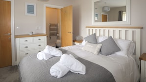 A bedroom with a bed, a bedside table, a mirror, a wardrobe, and a towel rack. - 4 Pen Llanw Tides Reach (Rhosneigr)