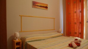 Una habitación de hotel con cama, mesita de noche, lámpara, un cuadro en la pared y cortinas naranjas.