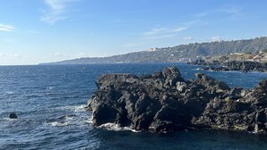 A coastal view with rocky formations and a distant hillside with buildings.