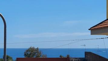 A coastal residential area with terracotta-tiled roofs, a clear blue sky, and a view of the sea.