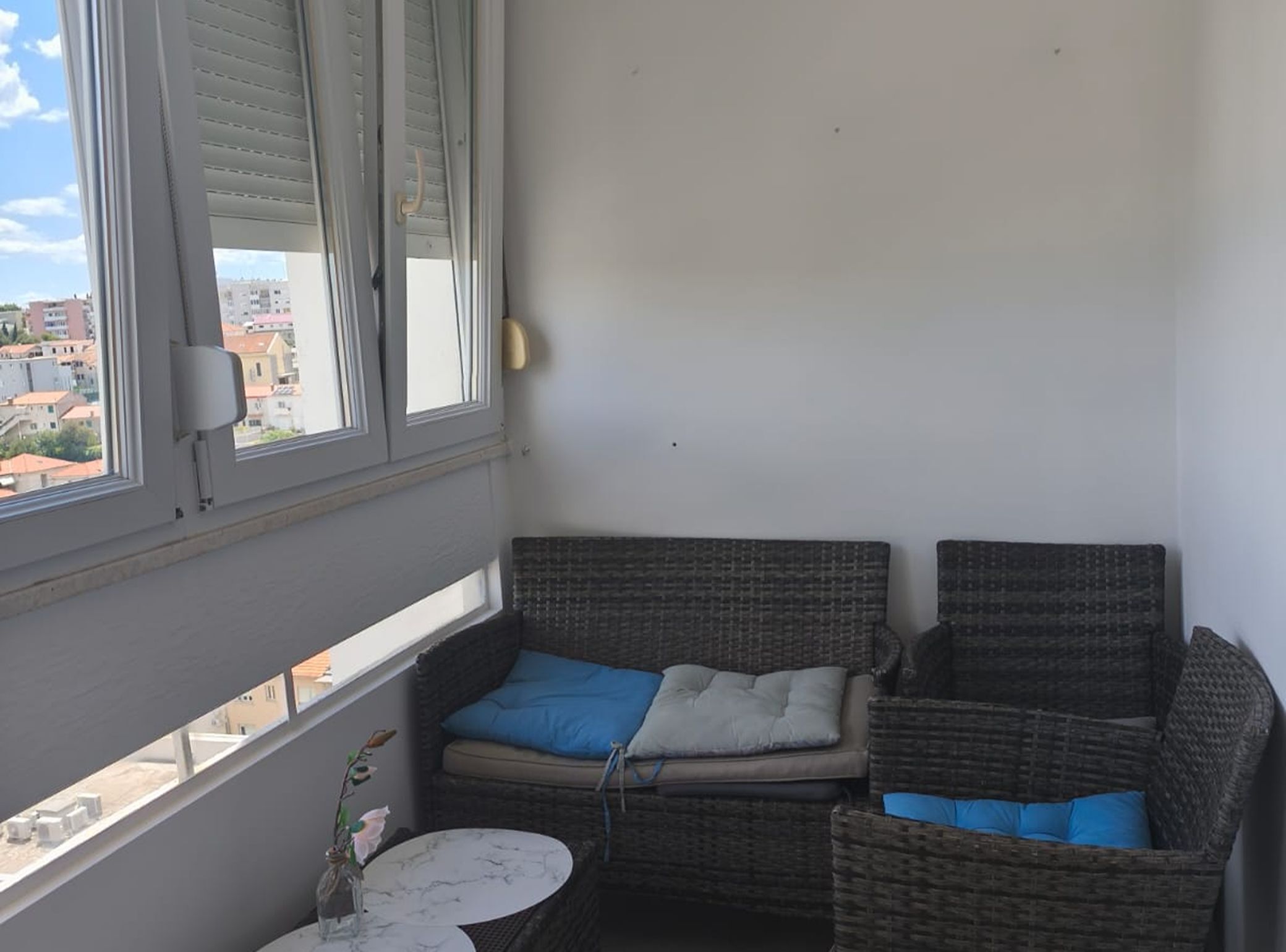 A balcony with wicker furniture, a small table, and a view of buildings.