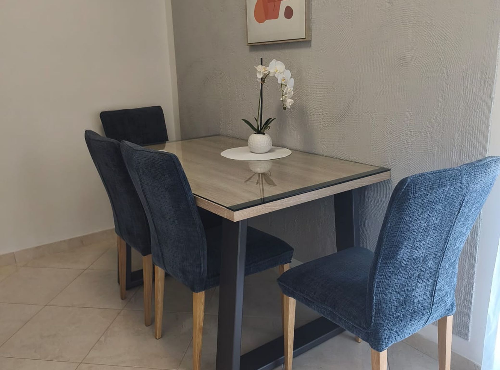 Un coin repas avec une table à plateau en verre, quatre chaises bleu foncé et une orchidée blanche dans un pot.