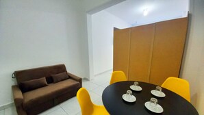 Une petite pièce moderne, avec un canapé marron, une table noire et quatre chaises, ainsi qu'une cloison blanche.