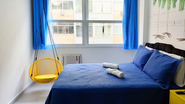 Une chambre à coucher avec un lit, un fauteuil suspendu et une fenêtre avec des rideaux.