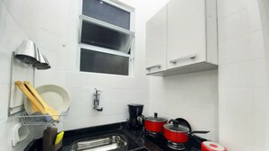 Une cuisine de taille réduite avec des meubles blancs, un plan de travail noir, une fenêtre et les appareils de cuisine de base.