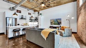 Una cocina moderna con una isla central, taburetes de bar y un sofá gris con una manta.