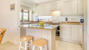 Una cucina moderna con mobili bianchi, un'isola centrale con sgabelli e un forno a incasso.