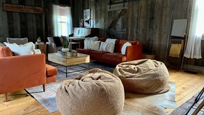 Una sala de estar acogedora con piso de madera, un sofá rojo, una mesa de centro de madera y dos pufs.