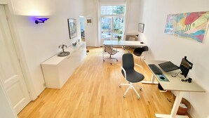 Una habitación moderna y luminosa con piso de madera, un escritorio con computadora, una silla de oficina negra y una mesa de comedor con sillas.