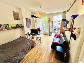 A compact living space with a bed, a desk with a computer, a couch, and a balcony with a view of the city. - Quiet 145m2  with garden in top location in centre-walk to major attractions ! (Amsterdam)