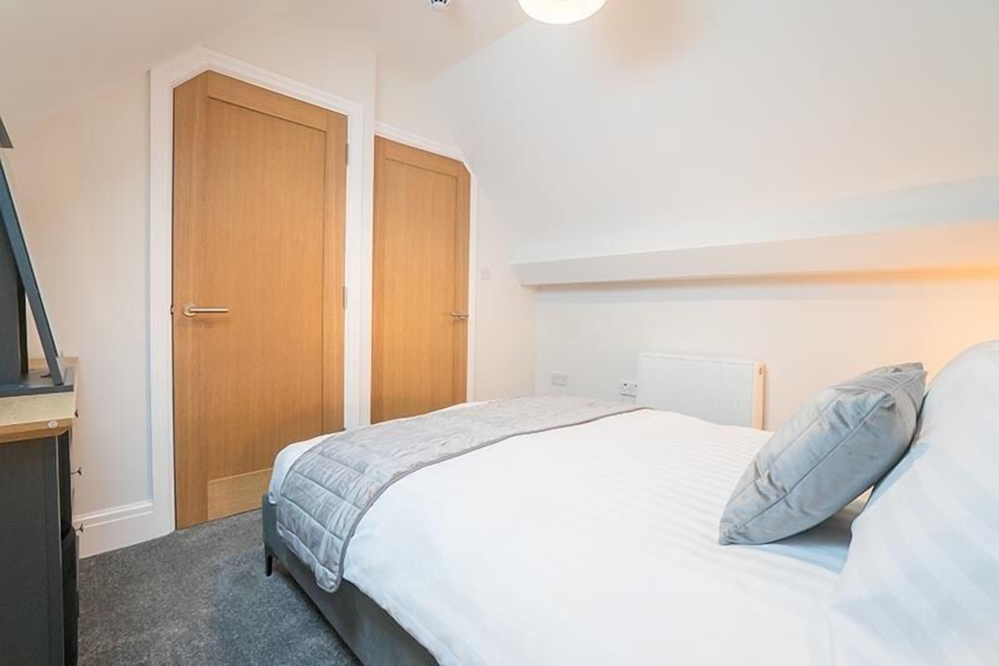 A bedroom with a bed, two wooden doors, a bedside table, and a nightstand.