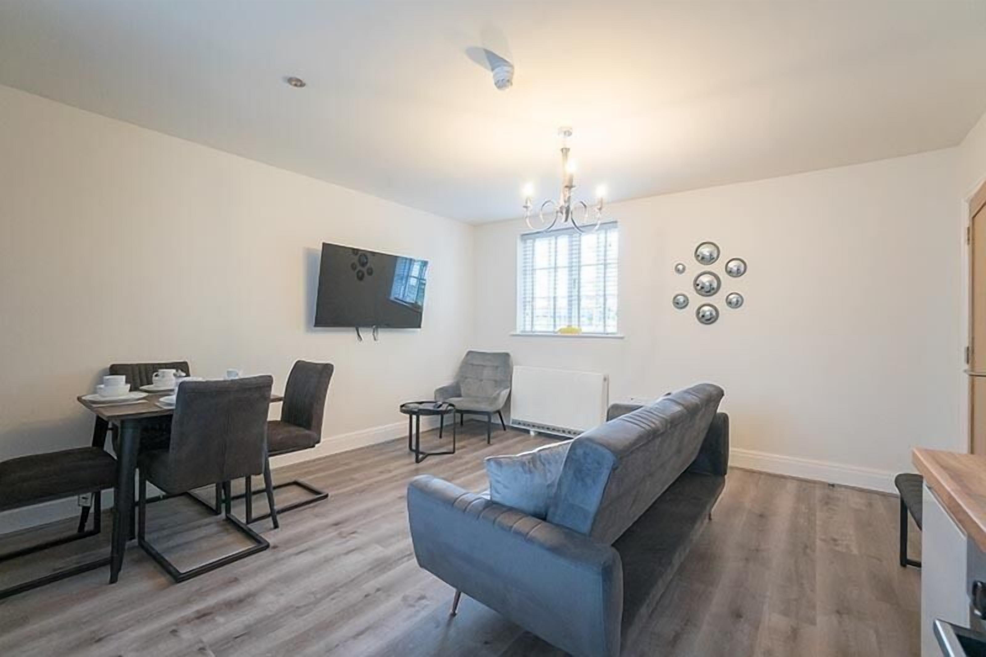 A modern living room with a sofa, chairs, a dining table, and a TV mounted on the wall.