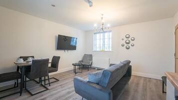 A modern living room with a sofa, chairs, a dining table, and a TV mounted on the wall.
