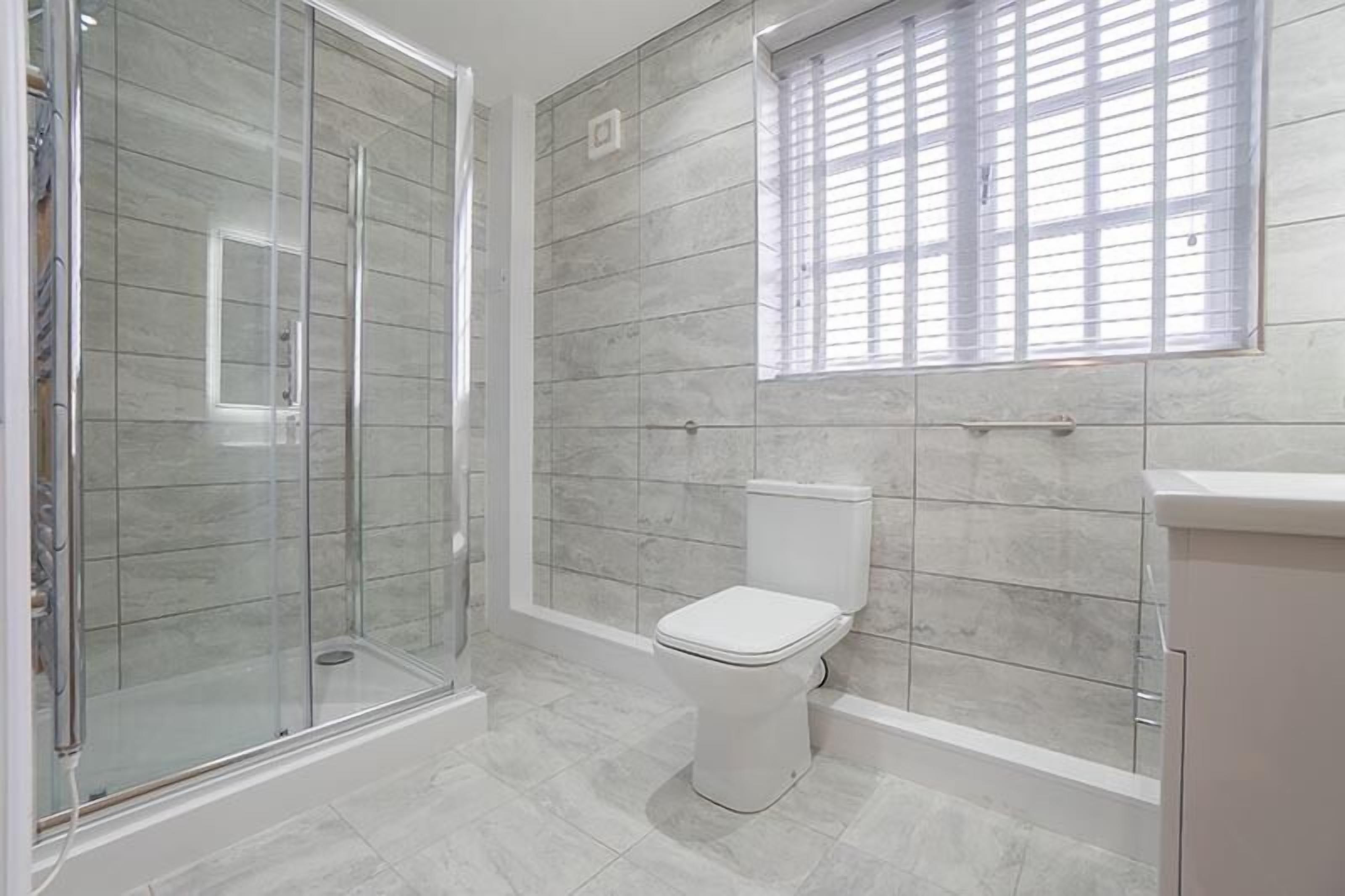 Un baño con ducha de vidrio, inodoro y ventana con persianas.