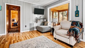 Un salon chaleureux avec un plancher en bois, un canapé, un téléviseur et une grande fenêtre.